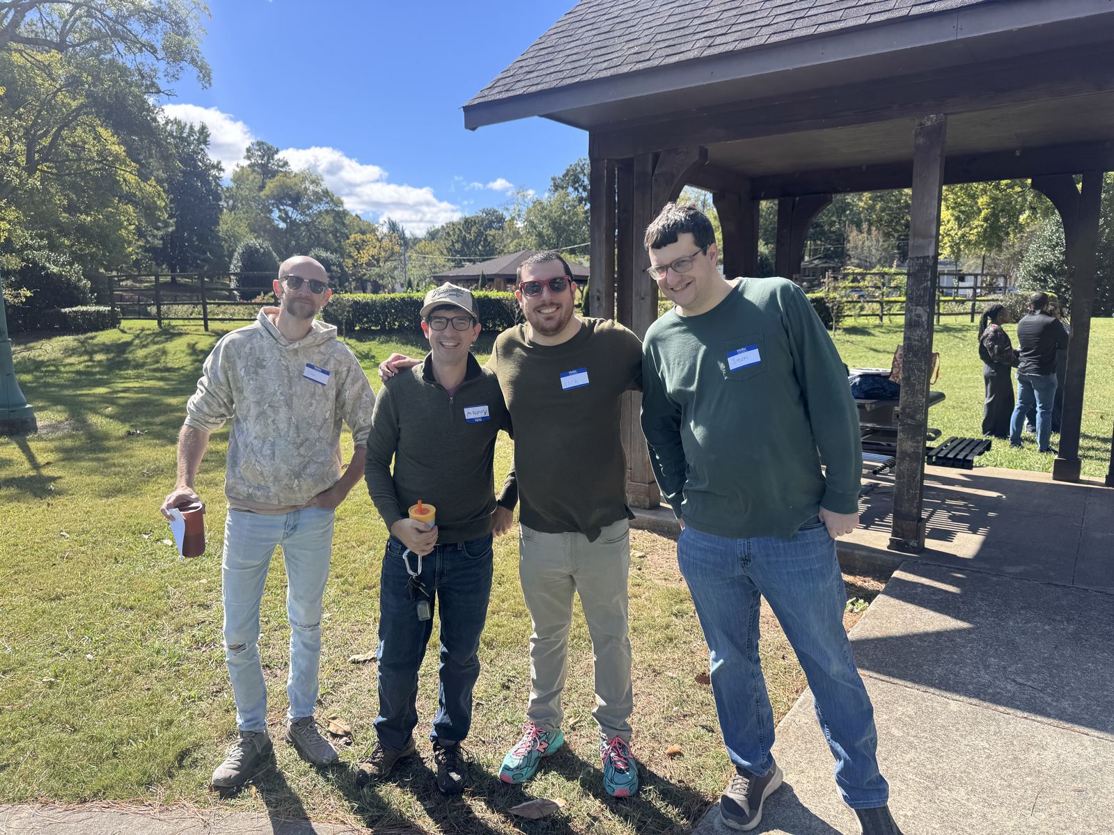 Four dads with name tags smiling together beside a park pavilion.